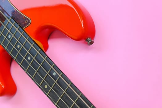Red electric bass guitar on a pink background. Close-up image.