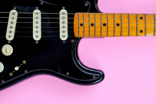 Black electric guitar on pink background. Top view with copy space.