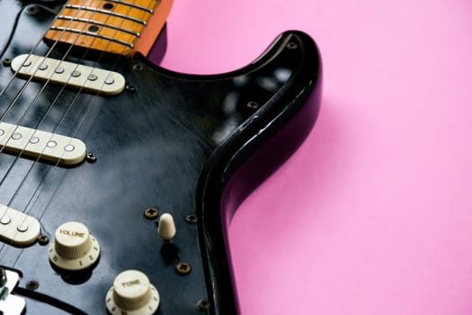 Black electric guitar on pink background. Top view with copy space.