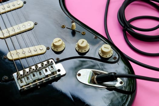 Electric guitar with cable on pink background, close-up image.