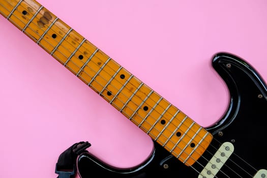 Black electric guitar on pink background. Top view with copy space.