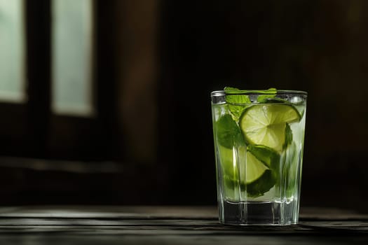 A refreshing mojito featuring slices of lime and fresh mint leaves is placed on a rustic wooden table in a softly lit room, creating a cozy atmosphere.