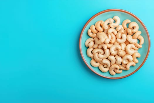 A turquoise plate is filled with golden roasted cashew nuts, showcasing their unique shape and texture against a vibrant solid backdrop.