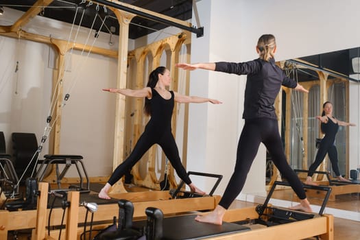 Two women standing on a reformer exercise machine perform an exercise in the gym.