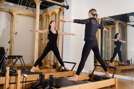 Two women standing on a reformer exercise machine perform an exercise in the gym.