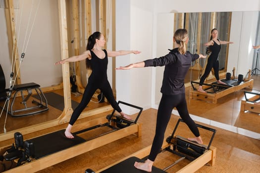 Two women standing on a reformer exercise machine perform an exercise in the gym.
