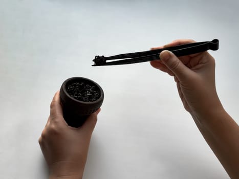Hands preparing hookah bowl with charcoal on white background.