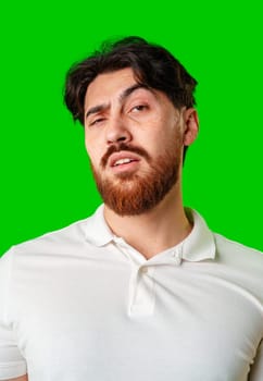 A young man with a beard showing a serious expression against a vibrant green background close up