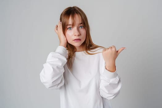 Young girl happily pointing against a neutral background while wearing a cozy white sweatshirt close up