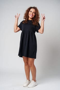 A young woman with curly hair poses cheerfully with peace signs in a neutral setting close up