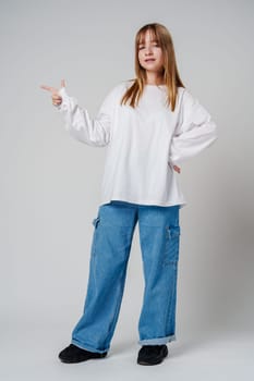 Young girl happily pointing against a neutral background while wearing a cozy white sweatshirt close up