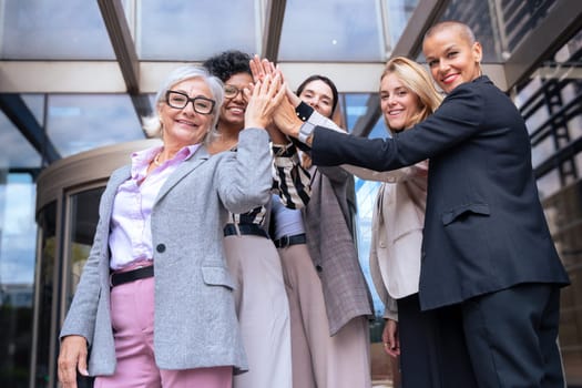 Five happy multiethnic women stacking hands in the city looking at camera