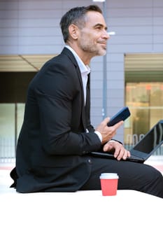 Mid adult man in a suit holds a phone in his hands, writes messages and reads news online, using an application