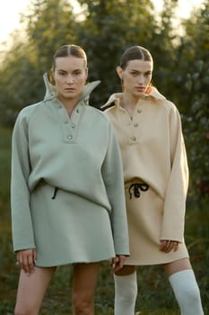 Two models in stylish tracksuits pose in apple orchard at sunset . The model is wearing a light-colored tracksuit and skirt.
