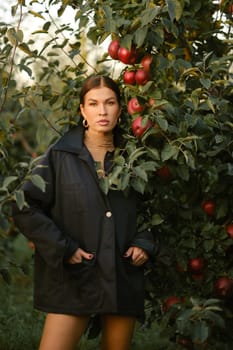 A beautiful girl in a black autumn jacket in an apple orchard. A fashionable girl at a fashion show in the apple orchard.