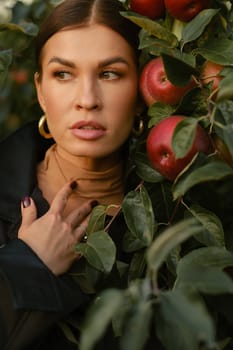 A beautiful girl in a black autumn jacket in an apple orchard. A fashionable girl at a fashion show in the apple orchard.