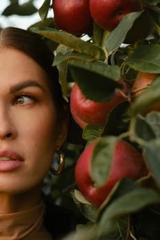 Close-up of a girl's face in an apple orchard. A fashionable girl on the background of a tree with red apples.