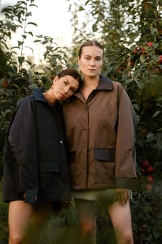 Two stylish girls in jackets at a fashion show in the apple orchard. Fashion show in the garden.