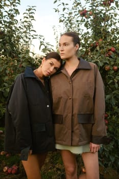 Two stylish girls in jackets at a fashion show in the apple orchard. Fashion show in the garden.