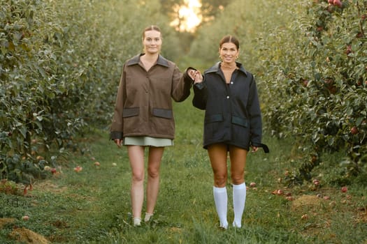 Two stylish girls in jackets at a fashion show in the apple orchard. Fashion show in the garden.