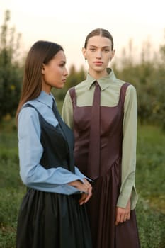 Two stylish girls in dresses with ties in the summer garden. Fashion show in nature.