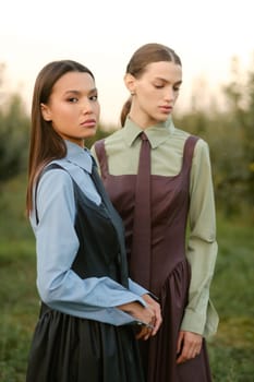 Two stylish girls in dresses with ties in the summer garden. Fashion show in nature.