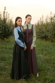 Two stylish girls in dresses with ties in the summer garden. Fashion show in nature.
