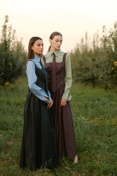 Two stylish girls in dresses with ties in the summer garden. Fashion show in nature.