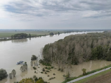 Stagno Lombardo, Italy - October 20th 2024 Aerial view of a river flooding the surrounding fields and forests after a heavy rain period, with the cloudy sky in the background