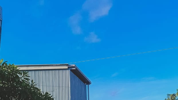 A warehouse and a tree under the blue sky. The warehouse placed beside a tree. The warehouse and the tree shined by the sun.