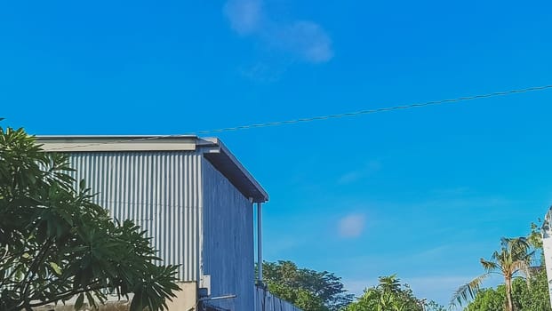 A warehouse and a tree under the blue sky. The warehouse placed beside a tree. The warehouse and the tree shined by the sun.
