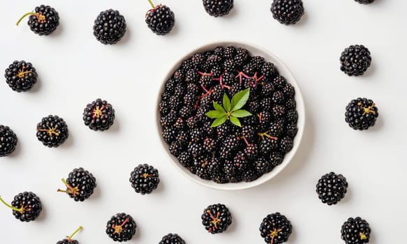 A bowl of blackberries is surrounded by individual blackberries on a white surface.