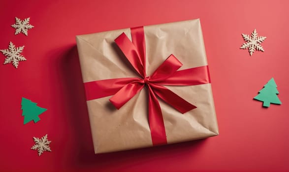 A brown, rectangular gift is wrapped in brown paper with a red satin ribbon tied in a bow. The gift is surrounded by red paper with small green and white Christmas-themed decorations.