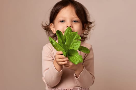 smiling child girl holding fresh green salad on beige background. focus on salad