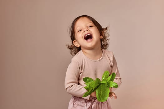 very excited smiling child girl holding fresh green salad on beige background. healthy baby food.