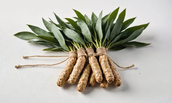 A bundle of turmeric roots, tied together with twine, lies on a white surface. The roots are brown and have a slightly rough texture. The leaves are green and have a smooth, glossy surface