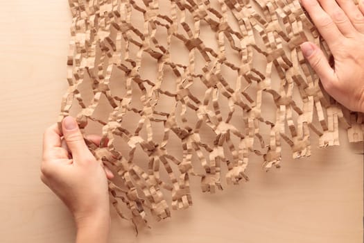 Environmentally friendly honeycomb paper in hands, hexagonal shape, strong elastic brown recycled cardboard paper for protective packaging, eco friendly reusable craft packing paper for moving or post delivery, close up background