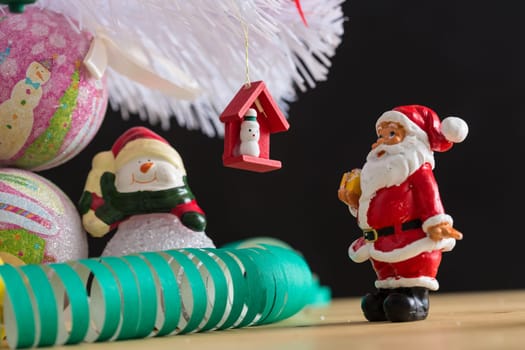 A small figurine of Santa Claus in a red and white suit holding a green sack, set against a blurred background. This festive ornament captures the spirit of Christmas.