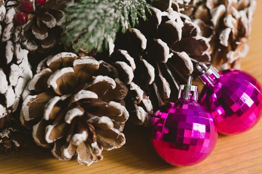 Holiday wreath adorned with snow-dusted pine cones, evergreen branches, red berries, and two shiny pink Christmas ornaments