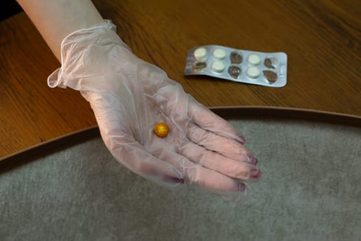 Hand in medical glove holds expired tablet brown color against background of plate of tablets that have lost their expiration date, monitoring suitability and freshness of medicaments
