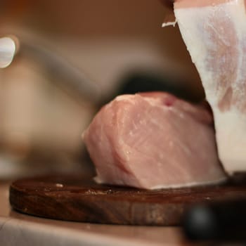 The chef cuts meat with a knife on a wooden board. A man's hand cuts a piece of meat with a knife. High quality photo