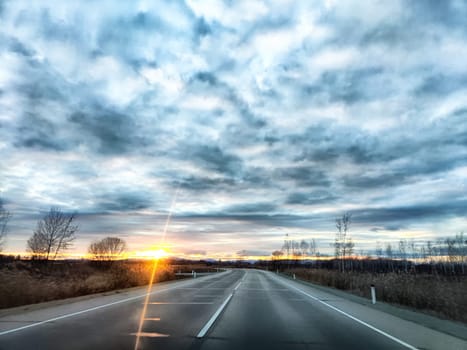 A beautiful sunset illuminates the horizon as clouds drift across the sky along a serene road.