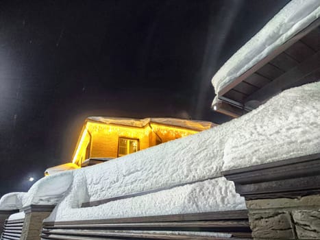 House decorated with bright Christmas garlands, surrounded by snow, under dark night sky