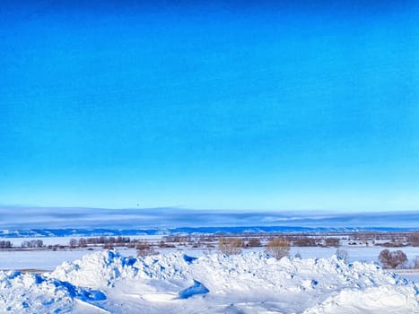 A vast expanse of snow blankets the ground, accented by a bright blue sky and distant mountains under winter sunlight.