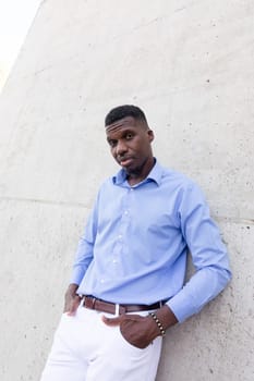 Portrait Of Handsome Stylish African American Man wearing White Jeans and Blue Shirt, Brown Belt Outdoor, Concrete Wall on Background. Fashionable Middle Age Male in His 40s,Ivorian. Vertical Plane