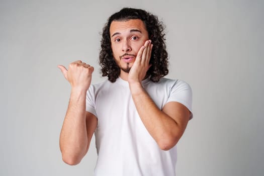 Young man in a white t-shirt and jeans pointing confidently while smiling in a studio setting close up