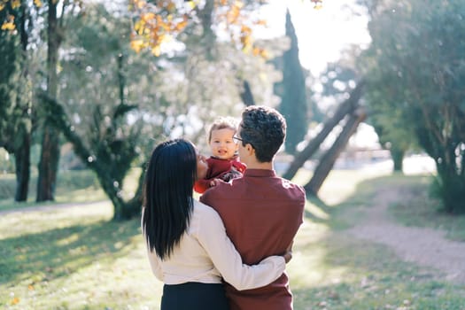Mom hugs dad kissing a little girl in his arms. Back view. High quality photo