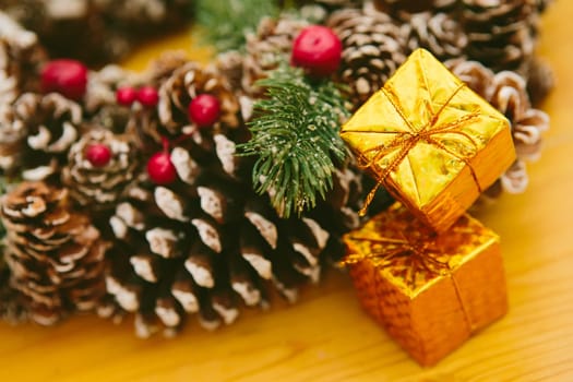 Small golden gift boxes stacked on a wooden surface, set against a blurred background of a festive Christmas wreath.