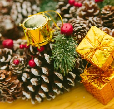 Small golden gift boxes stacked on a wooden surface, set against a blurred background of a festive Christmas wreath.