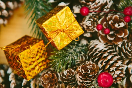 Small golden gift boxes stacked on a wooden surface, set against a blurred background of a festive Christmas wreath.